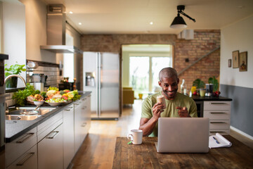 Middle aged african american food blogger and nutritionist promoting a health supplement and vitamin pills or tablets to his audience over a stream or video call on his laptop in the kitchen