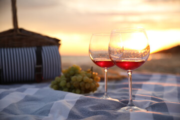 Blanket with glasses of wine and food on beach at sunset. Romantic picnic for couple