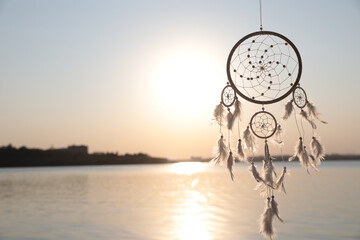 Beautiful handmade dream catcher near river at sunset. Space for text
