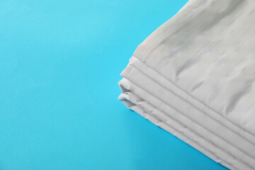 Stacked clean bed linens on light blue background, space for text
