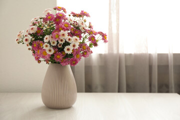 Beautiful flowers in vase on white wooden table at home, space for text