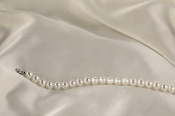 Beautiful pearl necklace on white silk, closeup. Space for text