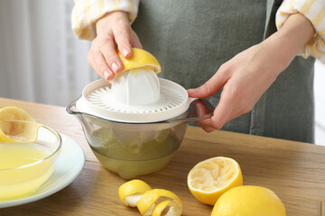 Woman with lemon using juicer at wooden table, closeup