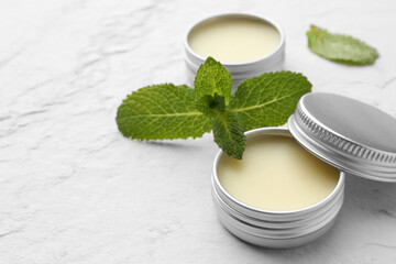 Mint lip balms and green leaves on beige textured table, closeup. Space for text