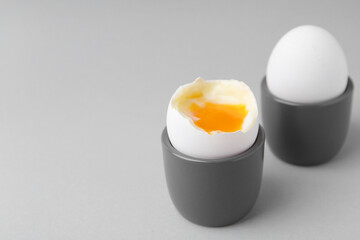 Soft boiled eggs in cups on light grey background, closeup. Space for text