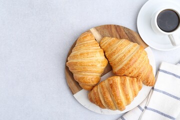 Tasty fresh croissants and cup of coffee on light grey table, flat lay. Space for text