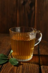 Refreshing green tea in cup and leaves on wooden table, closeup