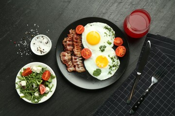 Tasty brunch. Delicious fried eggs, bacon, salad and glass of juice served on black table, flat lay
