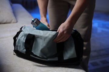 Man putting bottle of water into gym bag indoors, closeup