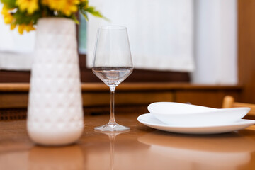 A delicate wine glass stands elegantly on a warm wooden table, accompanied by a neatly stacked dinner plate and soup plate.