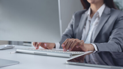 Fototapeta premium Business woman working on computer at desk in office for online research, reading email or report. Female entrepreneur person with internet connection, typing on computer keyboard, closeup