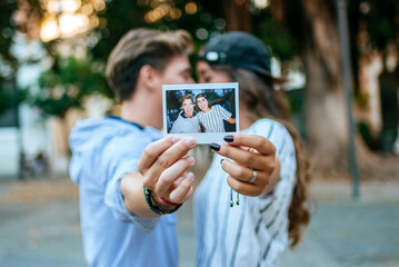 Young couple kissing and showing instant photo of themselves