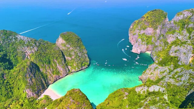 Aerial panoramic beautiful view of Phi phi island ring of steep limestone cliff hills surrounding Maya Bay white beaches and coral reefs around, boats floating nearby.
