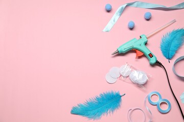 Hot glue gun and handicraft materials on pink background, flat lay. Space for text