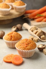 Tasty carrot muffins, fresh vegetables, sugar and walnuts on light grey table, closeup