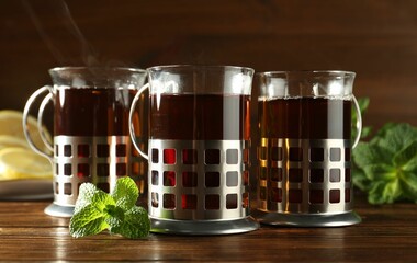 Glasses of hot tea in holders, mint and lemon on wooden table
