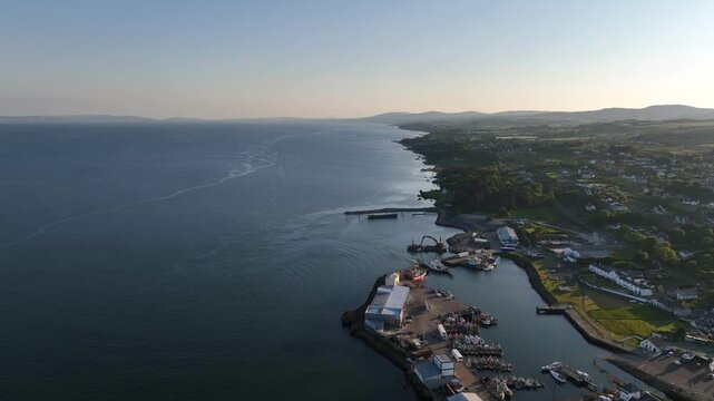 Lough Foyle Ferry, County Donegal, Ireland, June 2023. Drone pulls backwards along Greencastle Harbour and shoreline in the evening light across the water from Northern Ireland.