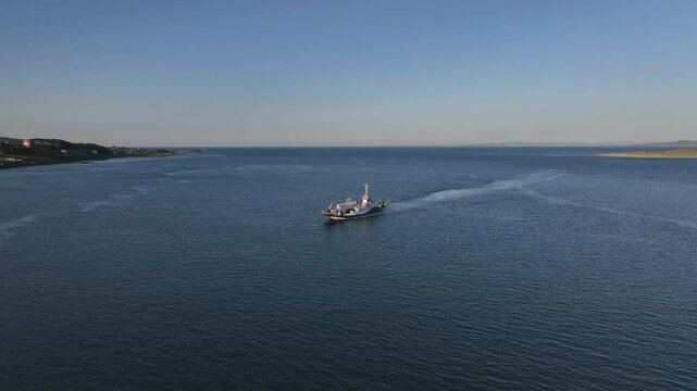 Lough Foyle Ferry, County Donegal, Ireland, June 2023. Drone pushes forwards tilting down to Bird's Eye View above a transport vessel returning from Magilligan Point as it leaves a wake on the water.