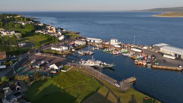 Lough Foyle Ferry, County Donegal, Ireland, June 2023. Drone orbits counter clockwise above Greencastle harbour as a vessel offloads cars and passengers, capturing the evening commuter activity.