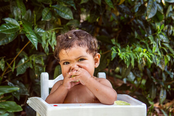 9-month-old baby eating lemon in his white highchair, outdoors.