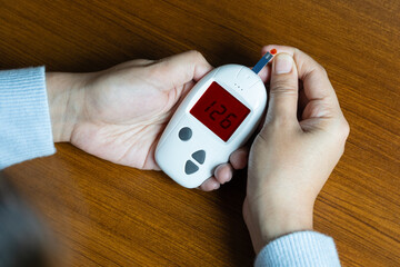 Woman's hands checking diabetes and hyperglycemia with digital blood sugar meter. Healthcare and...