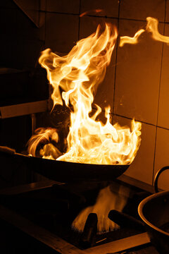 Foto espectacular de un sart&eacute;n flameando con comida, mostrando la t&eacute;cnica del flamb&eacute; en acci&oacute;n. Ideal para proyectos relacionados con gastronom&iacute;a, cocina profesional o publicidad de restaurantes.