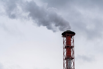 Red and white pipe with metal stocks and thick smoke against the background of a cloudy sky.