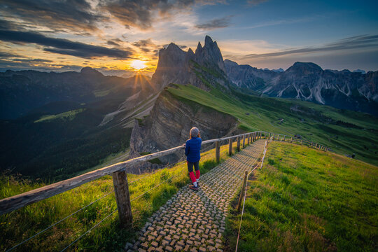 A woman in blue sweater is taking a sunrise at seceda viewpoint (dolomites, Italy)