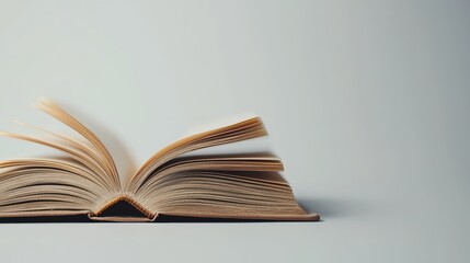 Obraz premium An open book rests on a flat surface, showcasing its pages. The minimalist background emphasizes the book's texture and details.