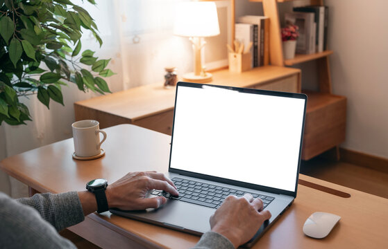 Close-up image of a man working on laptop computer at a table, typing on the laptop keyboard. the laptop with a white screen mockup