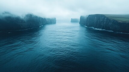Serene coastal cliffs shrouded in mist, overlooking a calm blue ocean under a cloudy sky