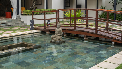 The SPA area. In the courtyard there is a swimming pool with a tiled bottom and stone sculptures. Wooden pedestrian bridge over the water. Terraces with sun loungers and curtains. Green vegetation.