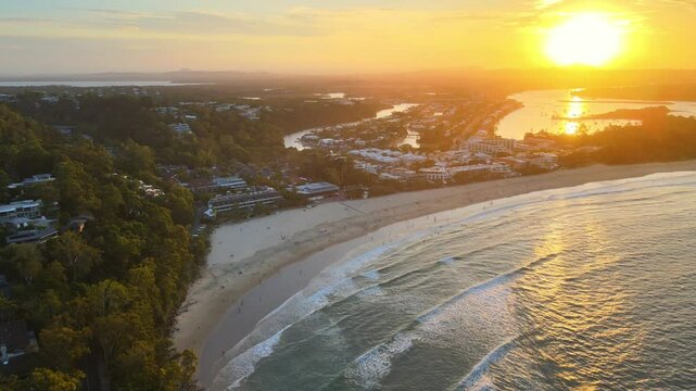 Aerial drone video of a breathtaking Noosa sunset, panning forward and upwards to reveal the golden hues over Noosa Main Beach and the stunning coastline