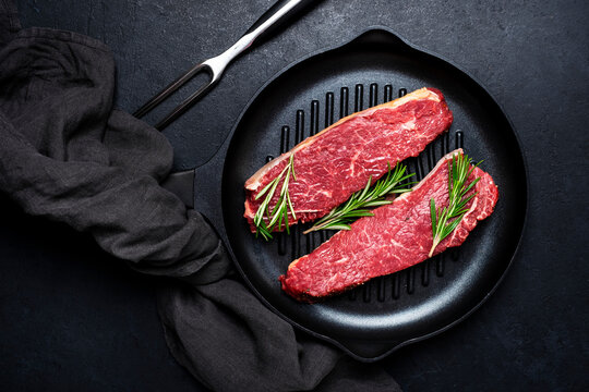Raw beef sirloin steaks with medium mamory with rosemary on grill pan. Black background, top view