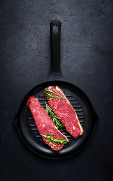 Raw beef sirloin steaks with medium mamory with rosemary on grill pan. Black background, top view