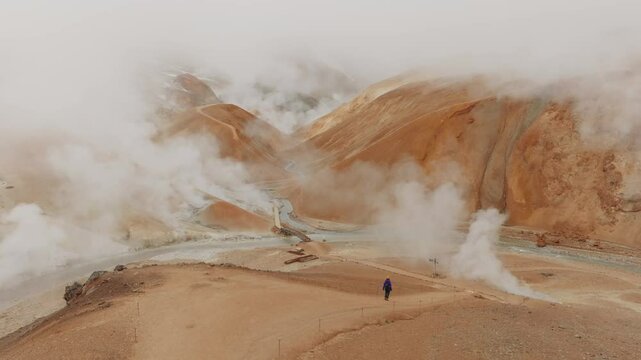 Aerial 50fps shot of Kerlingarfj&ouml;ll&rsquo;s geothermal area. Steam rises from orange hills, intersected by a winding river and a narrow bridge. Ideal for nature, travel, or geological projects.