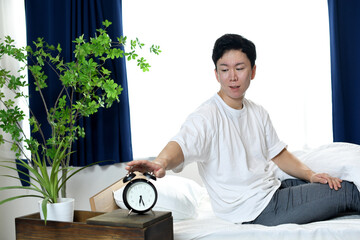 不機嫌な表情で目覚まし時計を止める男性