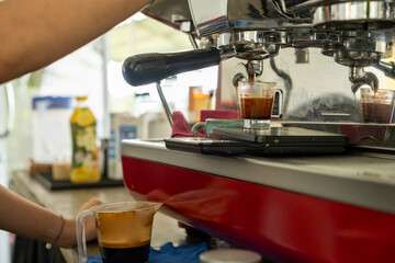 Close-up of a professional espresso machine brewing fresh coffee into a glass measuring cup. The scene captures the rich crema and the precision of barista techniques in a modern café setting.