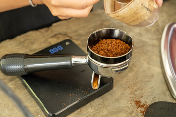 Close-up of freshly ground coffee being spooned into a portafilter, highlighting the rich texture and preparation process for brewing espresso, captured in a warm, inviting setting.