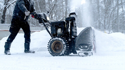 A man picks up snow on the street with a snow blower