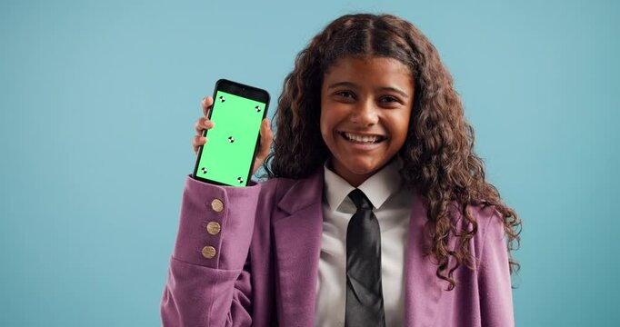 Green screen, phone and face of child in studio for online education, mockup space and advertising. Happy, blue background and portrait of girl on smartphone in school uniform for elearning website