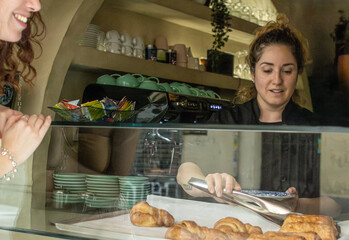 Obraz premium Female barista serves a croissant at a vegan coffee shop while the customer waits excitedly
