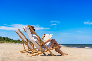 Summer holidays on beach with book. Beautiful mature women reading book sitting on beach chair on...