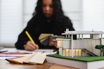 Modern eco-friendly house model with wood substitute material samples on architect desk office...