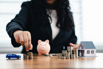 Woman stacks coins near a piggy bank, house, and car, financial planning, savings, and investment...