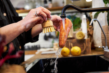 a woman in the kitchen washing vegetables and carrot  with a wooden brush, in a modern black sink