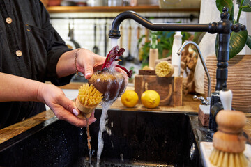 a woman in the kitchen washing vegetables and beets with a wooden brush, in a modern black sink