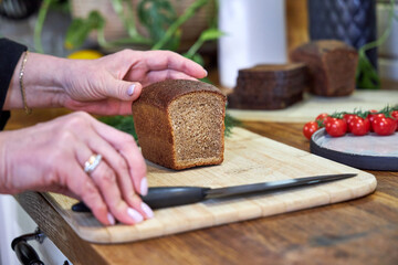 a woman slices rye gray bread on a wooden countertop in the kitchen