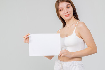 Pretty young brunette standing with a A4 empty paper sheet on a white background. Copyspace