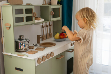 cute toddler blonde baby girl playing on toy kitchen at home,